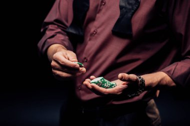 selective focus of man holding poker chips on black  clipart