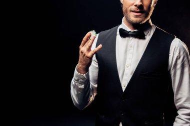 cropped view of man in formal wear holding poker chip isolated on black  clipart