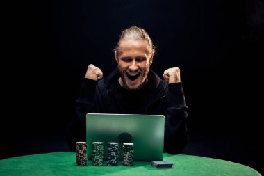 Kyiv, Ukrayna - 20 Ağustos 2019: siyah üzerine izole edilmiş poker çipleri yanında dizüstü bilgisayar kullanan mutlu adam. 