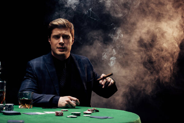 handsome man holding cigar while smoking on black with smoke 