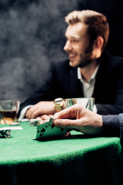 KYIV, UKRAINE - AUGUST 20, 2019: selective focus of man touching playing cards near player on black with smoke
