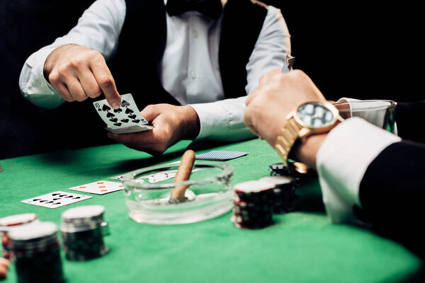 КИЕВ, УКРАИНА - 20 августа 2019 года: обрезанный вид человека возле крупье с игральными картами, изолированными на черном
 