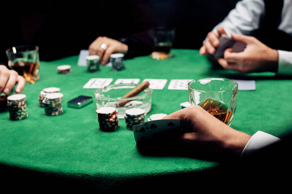 KYIV, UKRAINE - AUGUST 20, 2019: cropped view of man holding playing cards near croupier isolated on black 