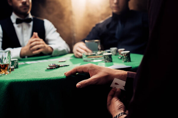 KYIV, UKRAINE - AUGUST 20, 2019: cropped view of man cheating while playing poker on black with smoke 