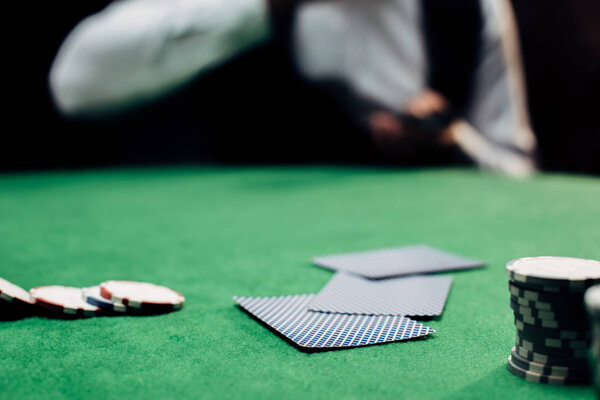 KYIV, UKRAINE - AUGUST 20, 2019: cropped view of man near playing cards and poker chips on poker table isolated on black 