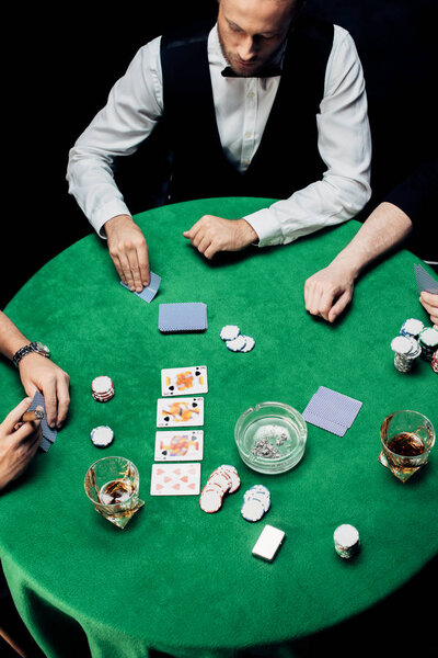 KYIV, UKRAINE - AUGUST 20, 2019: top view of men playing poker near croupier isolated on black 