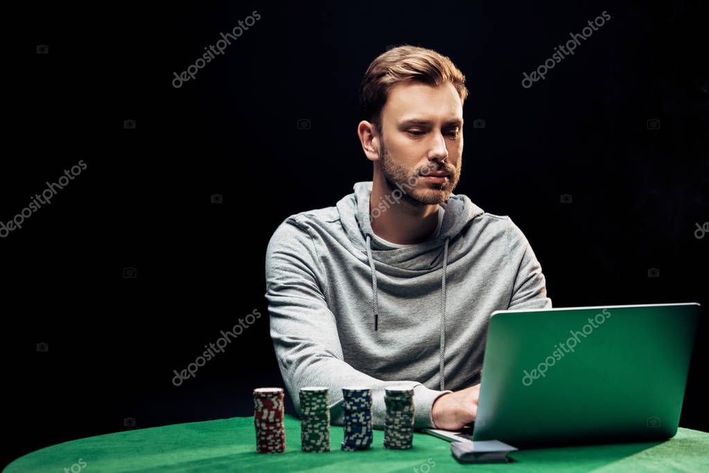 KYIV, UKRAINE - AUGUST 20, 2019: handsome man using laptop near playing cars isolated on black
