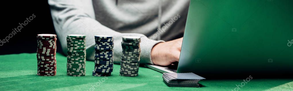 KYIV, UKRAINE - AUGUST 20, 2019: panoramic shot of man using laptop near poker chips isolated on black
