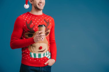 Noel Baba şapkalı ve Noel süveterli bir adamın mavi üzerine izole edilmiş kahve tutarken çekilmiş görüntüsü.