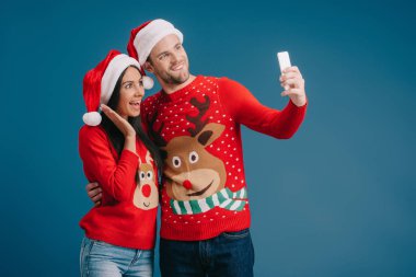 santa şapkave noel kazak mavi izole akıllı telefon selfie alarak heyecanlı çift