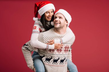 noel zamanında noel şapkası içinde gülümseyen adam piggybacking kız arkadaşı kırmızı izole