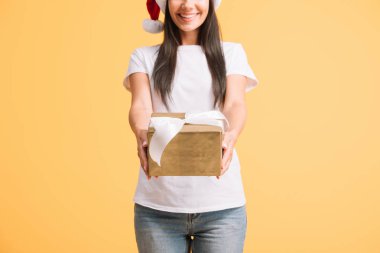 sarı izole noel hediye kutusu tutan santa şapka gülümseyen kadın kırpılmış görünümü