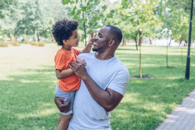 cheerful african american holding adorable son touching his nose  clipart