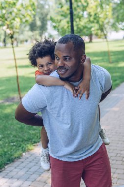 Genç Afro-Amerikan babası parkta yürürken tatlı oğlunu sırtında taşıyor.