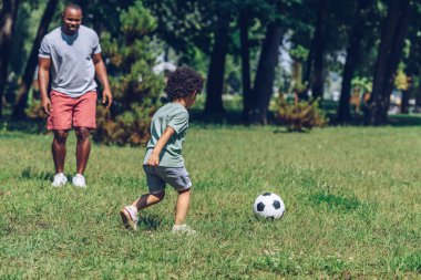 Genç Afrikalı Amerikalı baba parkta oğluyla futbol oynuyor.