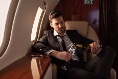 Takım elbiseli yakışıklı adam uçakta şampanyayı cama döküyor.
