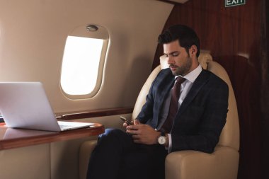 İş gezisi sırasında uçakta akıllı telefon ve laptop üzerinde çalışan işadamı 