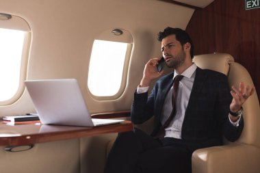 Yönetici iş gezisi sırasında bilgisayarla uçakta akıllı telefondan konuşuyor. 
