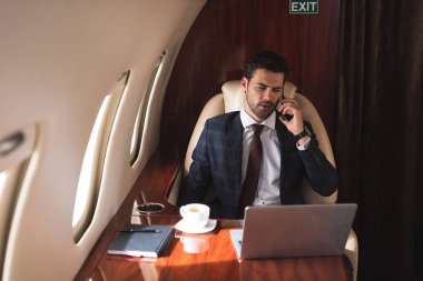 Erkek lider iş gezisi sırasında uçakta dizüstü bilgisayarla konuşuyor. 