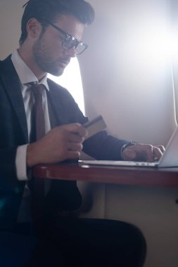 Uçakta kredi kartı ve dizüstü bilgisayarı olan yakışıklı bir iş adamı