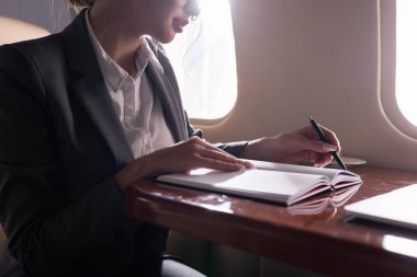 cropped view of businesswoman working with documents in plane during business trip clipart