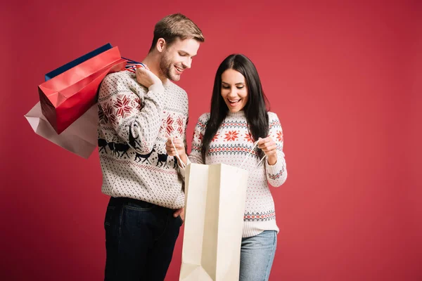 Casal Sorridente Camisolas Inverno Olhando Sacos Compras Isolados Vermelho — Fotografia de Stock