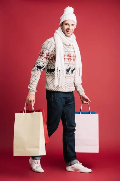 冬のスカーフ 帽子とセーターでハンサムな男は 買い物袋で歩いて 赤で孤立 — ストック写真