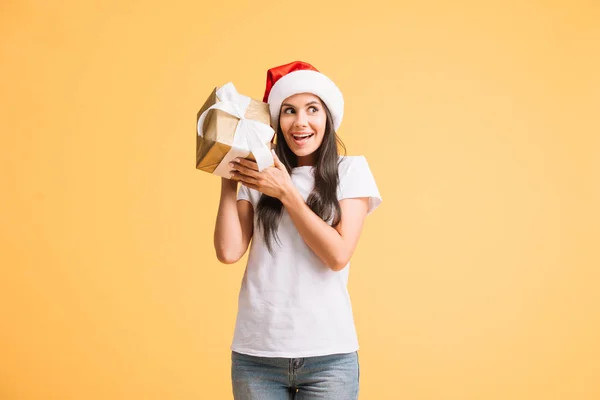 黄色に隔離されたクリスマスギフトボックスを保持するサンタ帽子で興奮若い女性 — ストック写真