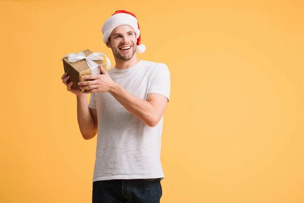 黄色に隔離されたクリスマスプレゼントを保持するサンタ帽子の陽気な男 — ストック写真