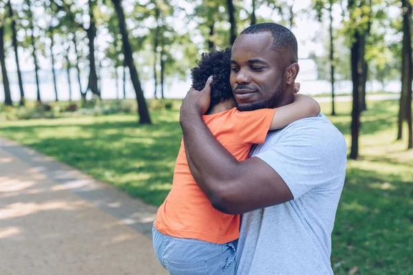 Mutlu Afro-Amerikan babası parkta sevimli oğlunu kucağına alıp kucaklıyor.