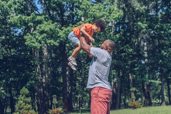 Jovem Afro Americano Homem Segurando Alegre Filho Acima Cabeça Enquanto — Fotografia de Stock