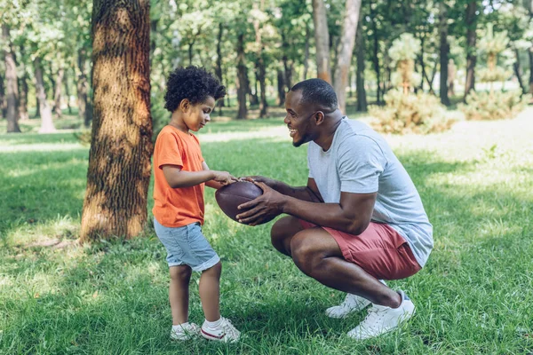 Bonito Afro Americano Homem Mostrando Rugby Bola Para Adorável Filho — Fotografia de Stock