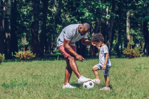 young african american father teaching son playing football in park