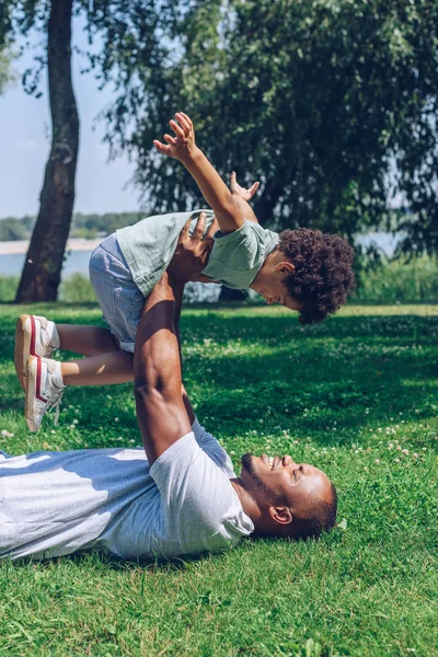 Mutlu Afro-Amerikan baba ve oğlu parkta çimenlikte eğleniyor.