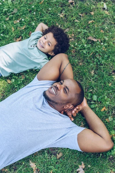 Feliz Pai Filho Afro Americano Deitado Gramado Enquanto Descansa Parque — Fotografia de Stock