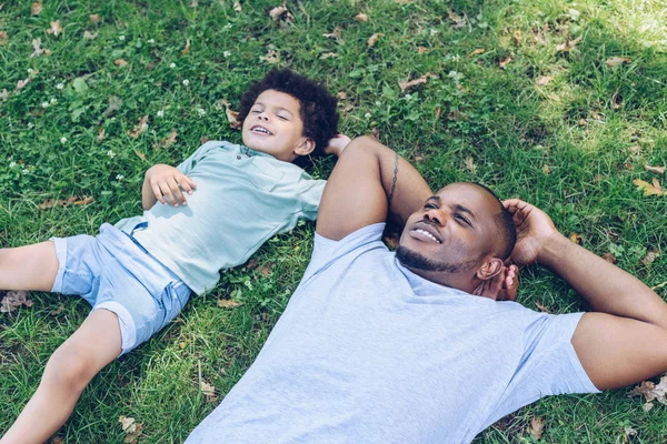 Sorrindo Afro Americano Pai Filho Deitado Gramado Enquanto Descansa Parque — Fotografia de Stock