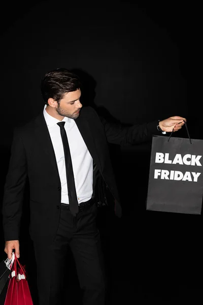 handsome man holding shopping bags with black friday sign, isolated on black