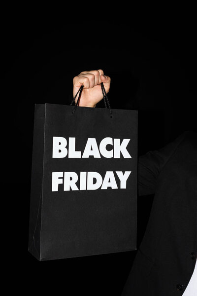 partial view of man holding shopping bag with black friday sign, isolated on black