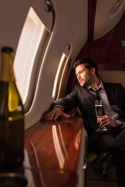 dreamy man holding glass of champagne in plane, selective focus of bottle 