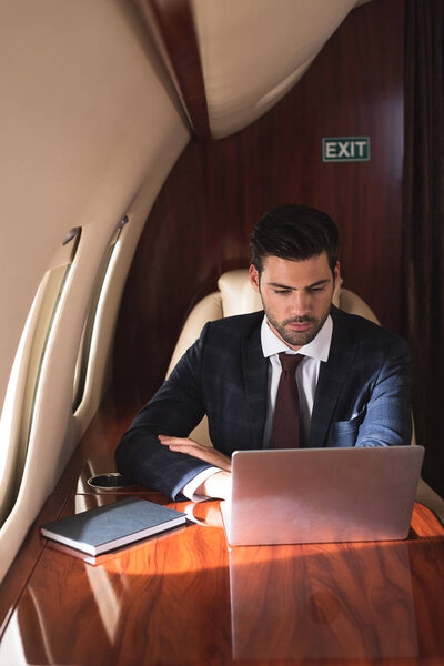 serious businessman working with laptop in plane during business trip 