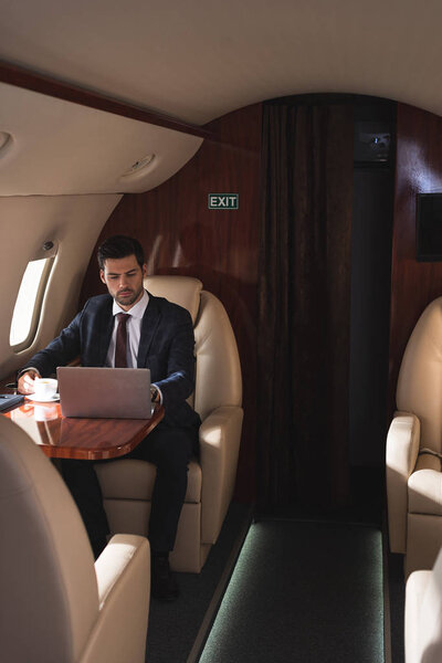 красивый бизнесмен, работающий на ноутбуке в самолете во время деловой поездки
 
