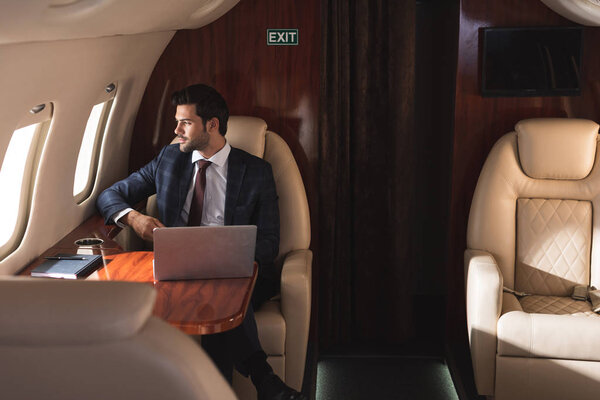 handsome businessman working with laptop in plane during business trip 