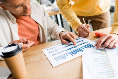 young businesspeople analyzing graphs and charts at workplace in office clipart