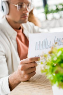 Genç işadamlarının seçici odak noktası kulaklıklarda oturmak ve grafik ve çizelgelerle kağıt analiz etmek.