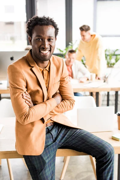 Lächelnder Afrikanisch Amerikanischer Geschäftsmann Sitzt Mit Verschränkten Armen Schreibtisch — Stockfoto