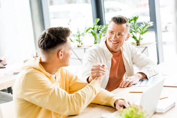 Twee Jonge Zakenmannen Schudden Elkaar Hand Terwijl Samen Werkplek Zitten — Stockfoto