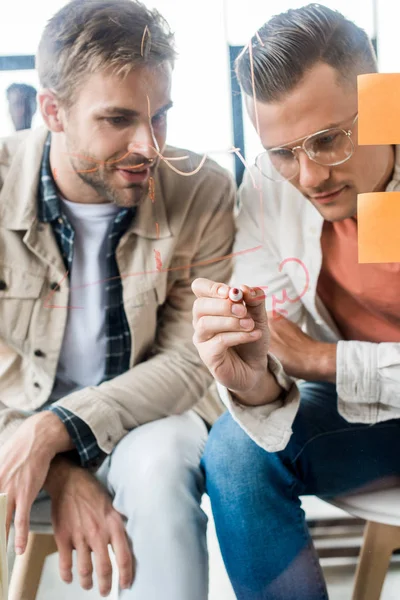 Joven Hombre Negocios Escribiendo Tablero Cristal Mientras Trabaja Con Colega — Foto de Stock