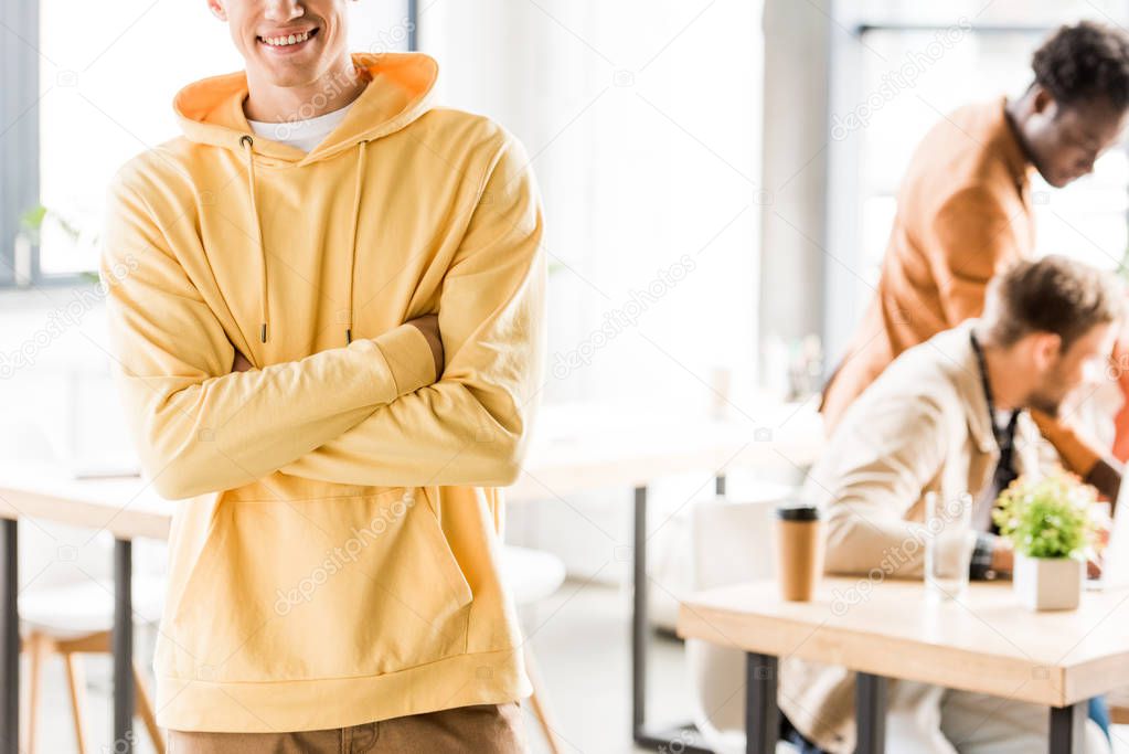 cropped view of young businessman in casual clothing standing with crossed arms near multicultural colleagues