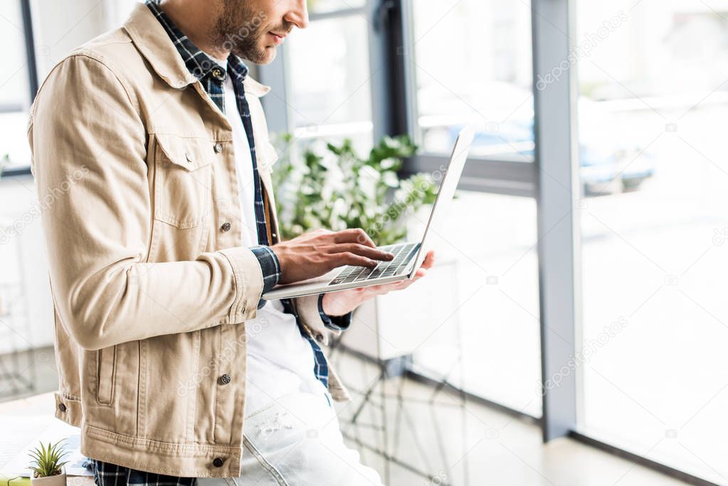 cropped view of young businessman using laptop in office