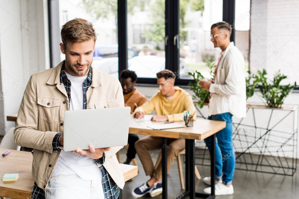 young businessman using laptop near multicultural colleagues working in office